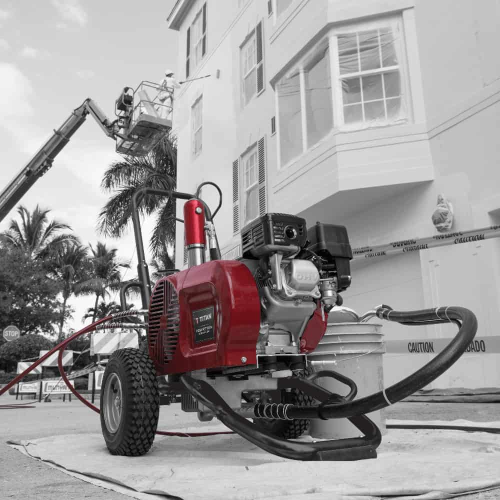 Red airless sprayer in front of a building with palm trees in the background
